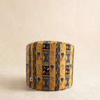 Golden African wax print drum pouf ottoman with Adinkra-inspired symbols on cream background — front-facing studio shot