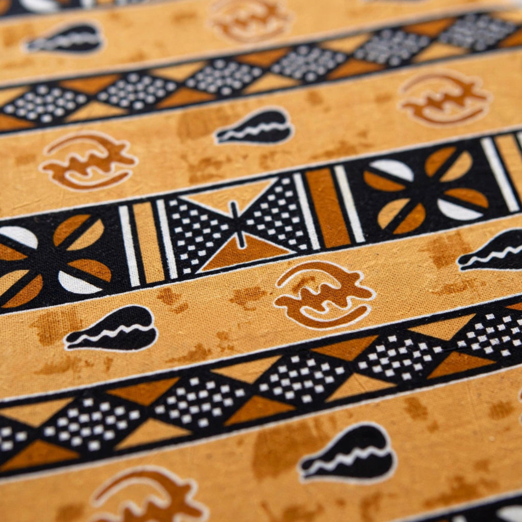 Close-up of golden amber African wax print fabric with hand-stamped Adinkra symbols and geometric stripe patterns in black, white, and copper