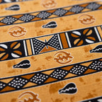 Close-up of golden amber African wax print fabric with hand-stamped Adinkra symbols and geometric stripe patterns in black, white, and copper
