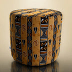 Handmade drum pouf ottoman in golden amber African wax print with black geometric symbols — front angled view