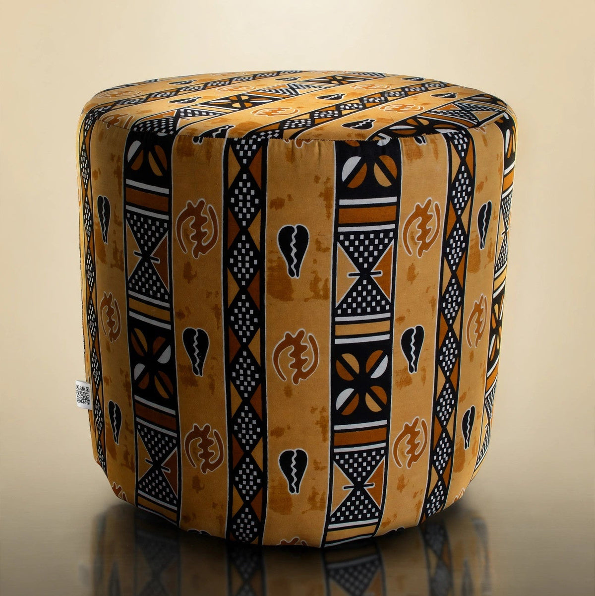Handmade drum pouf ottoman in golden amber African wax print with black geometric symbols — front angled view