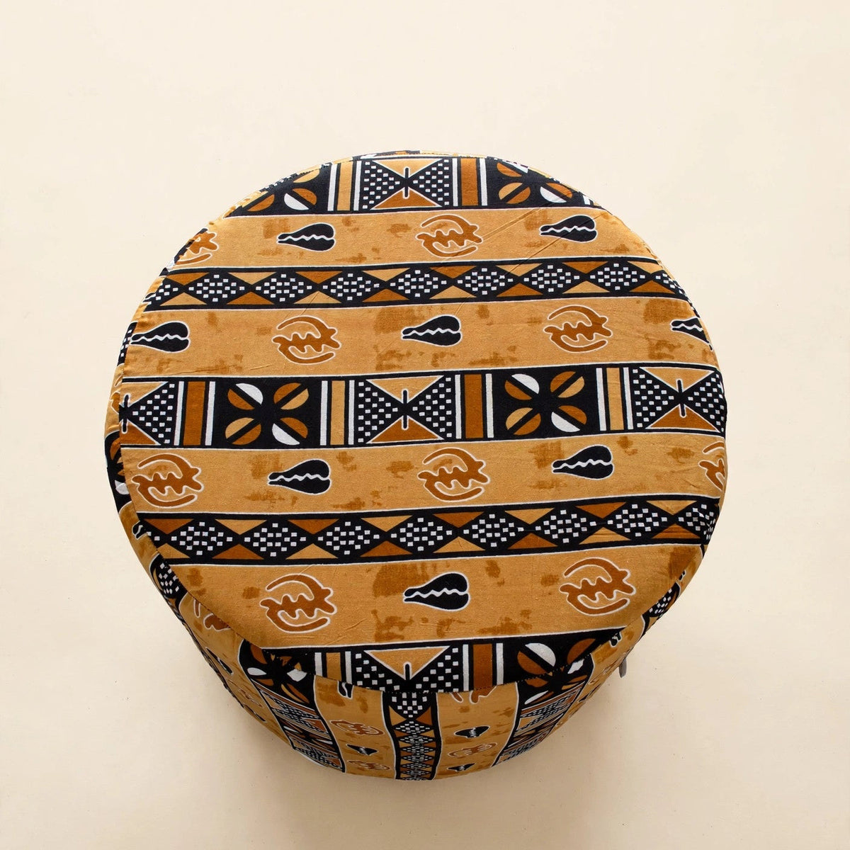Top-down view of the Drum Pouf ottoman in golden African wax print with horizontal stripe patterns and Adinkra symbols