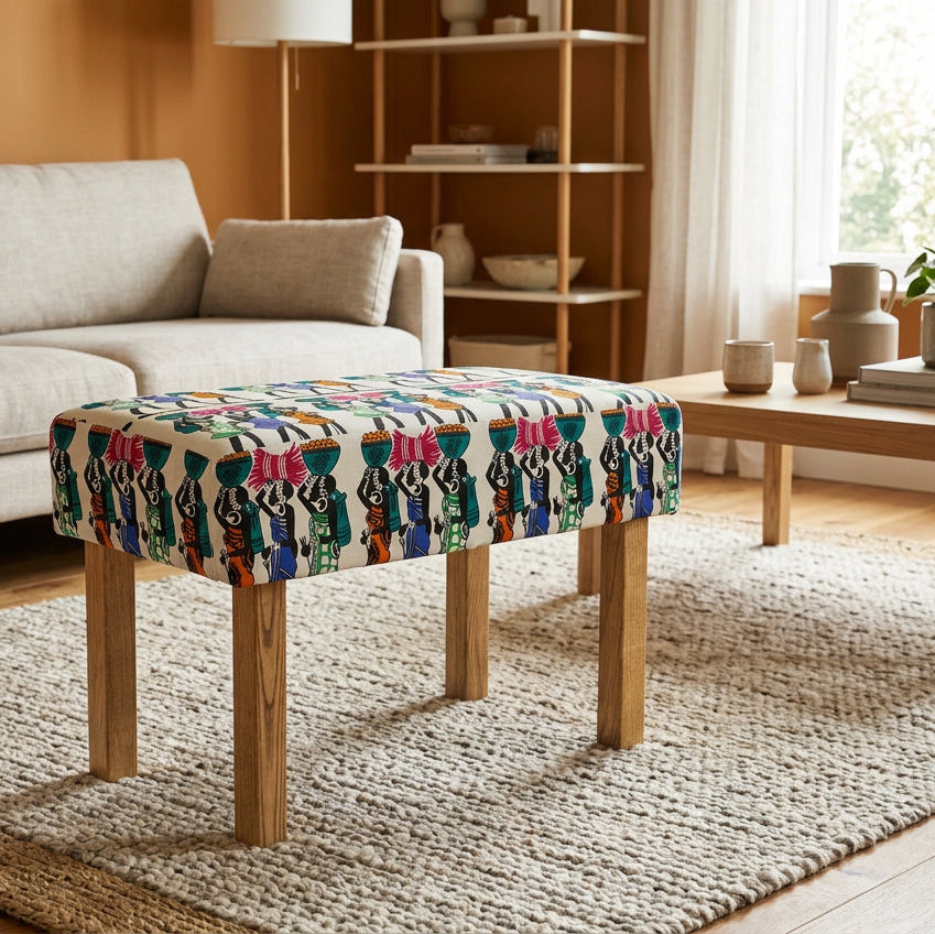 A square upholstered bench with a colorful geometric pattern on the top and natural wood legs, styled in a modern living room setting.
